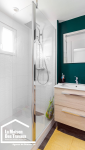 salle de bain vert de face avec lavabo en bois clair douche a l'italienne blanc 