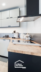 Plan de travail en bois avec plaque de cuisson intégrée, crédence noire mate et meubles hauts épurés dans une cuisine rénovée en Haute-Savoie.