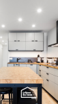 Cuisine contemporaine avec îlot central en bois massif, rangements minimalistes gris clair et hotte noire design – projet en Haute-Savoie.