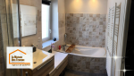 Salle de bain rénovée avec carrelage mural texturé, baignoire d’angle et meuble vasque suspendu.
