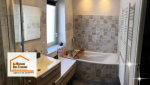 Salle de bain rénovée avec carrelage mural texturé, baignoire d’angle et meuble vasque suspendu.