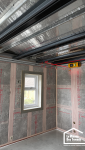 Détail technique d'un chantier d'extension avec pose d'isolation en laine de verre et rails métalliques.