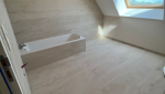 Vue d’ensemble de la salle de bain après rénovation avec baignoire et travertin