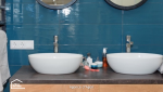 Détail d’une salle de bain rénovée à Agen : miroir rond, carrelage bleu et sèche-serviettes noir.