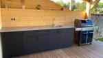 Alliance du bois et du mobilier noir pour cette cuisine d'été moderne réalisée sur une terrasse en bois à Coublevie.