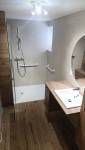 Salle de bain rénovée à Charancieu avec douche accessible, barres de maintien, meuble vasque et finitions effet bois.