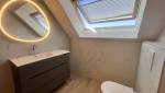 Salle de bain rénovée sous combles avec meuble vasque suspendu et miroir rétroéclairé.