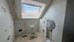 Salle de bain sous pente en cours de rénovation avec carrelage grand format effet marbre et fenêtre de toit.