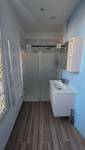 Salle de bains moderne rénovée avec meuble vasque blanc, miroir rond et douche vitrée
