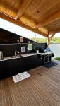 Cuisine d'été sur mesure finalisée à Coublevie avec rangements intégrés, évier, plan de travail et barbecue sous terrasse couverte.