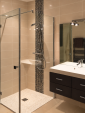 Une douche aux parois transparentes et un meuble vasque à quatre tiroirs composent cette salle de bain rénovée, avec une faïence beige rehaussée de mosaïque.