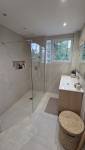 Douche à l’italienne avec paroi vitrée transparente, carrelage beige, niche murale de rangement et robinetterie dorée.