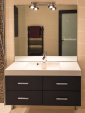 e meuble vasque dispose de quatre tiroirs pour organiser les affaires de toilette. Un grand miroir et un éclairage mural complètent cet espace.