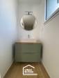 Meuble vasque suspendu vert sauge avec plan effet bois et miroir rond dans une salle d'eau à Damgan