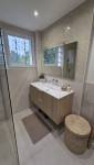 Meuble vasque suspendu effet bois avec plan blanc, grand miroir, carrelage beige et accessoires naturels dans une salle de bains moderne.
