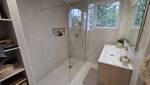 Salle de bains moderne avec douche à l’italienne vitrée, meuble vasque effet bois, carrelage beige et rangements intégrés.