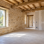 Intérieur d’une maison en pierre en cours de rénovation, avec poutres apparentes et cloisons en placo ».